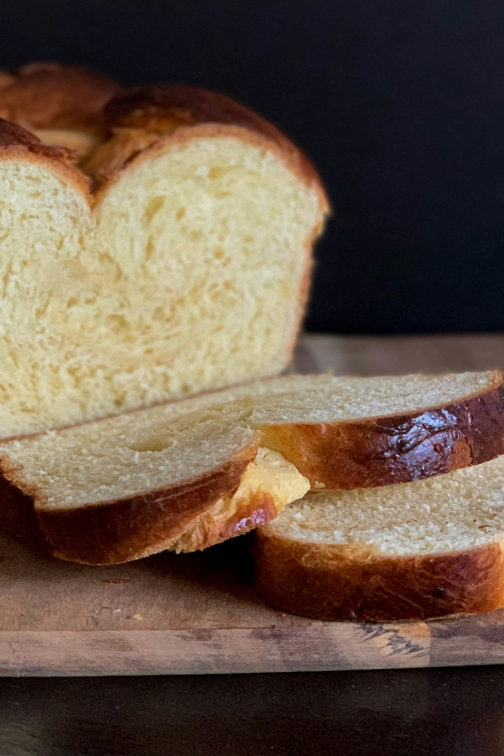 Un pain brioché tranché, révélant une mie tendre et moelleuse avec une croûte dorée et brillante, posé sur une planche en bois avec un fond sombre.