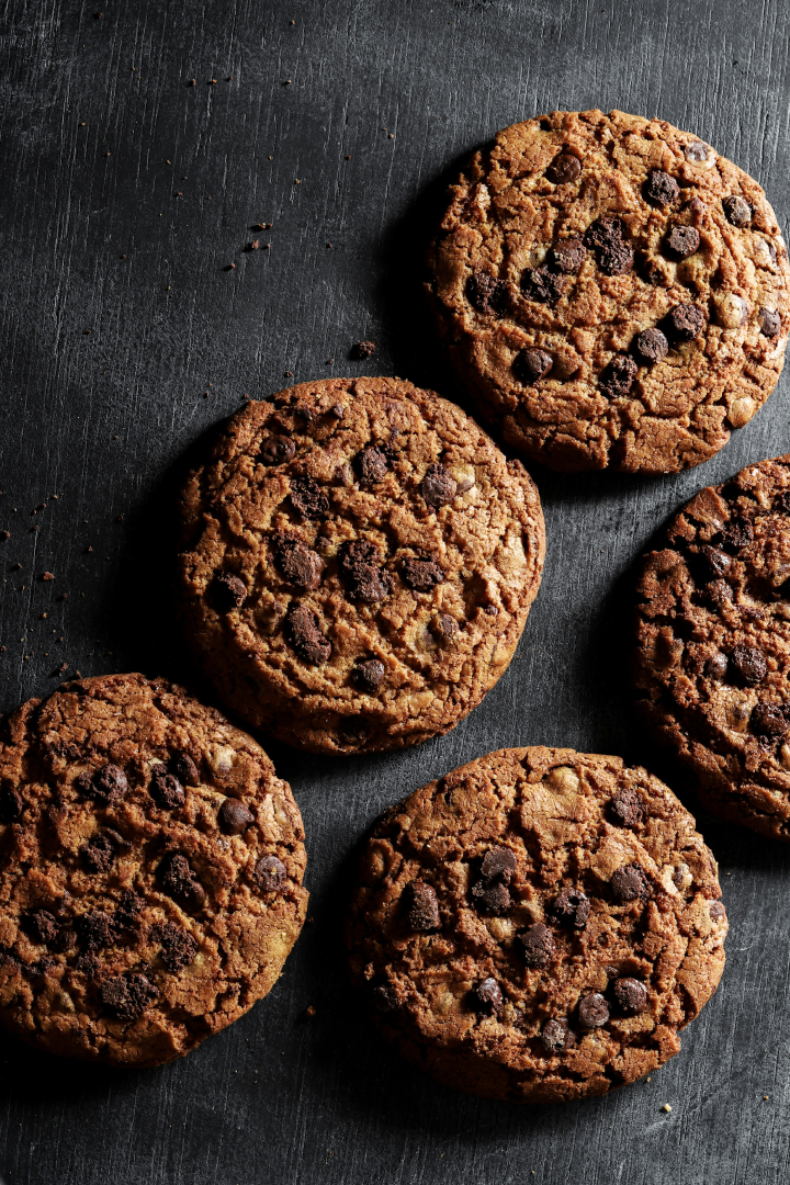 Des cookies aux pépites de chocolat disposés sur une surface sombre, montrant leur texture croustillante et appétissante.