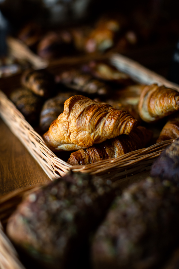 Un panier en osier rempli de croissants dorés et croustillants, avec d'autres viennoiseries en arrière-plan.